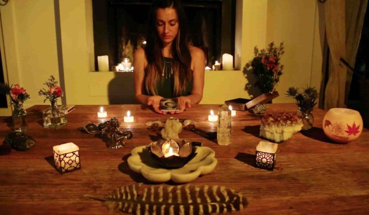 Woman chanting at her altar covered in sweet smells, candle flames, and sacred enchantments