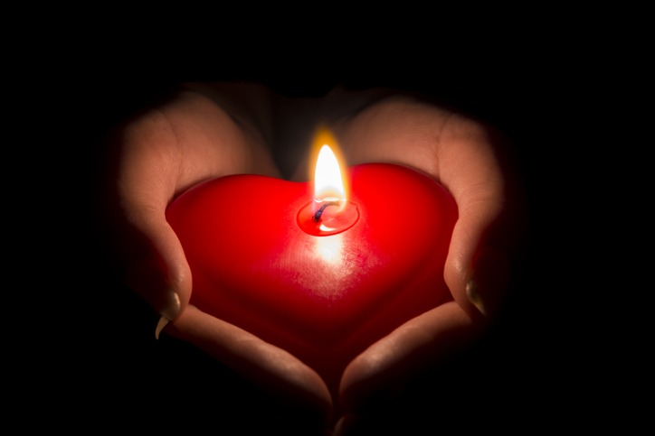 womans hands holding a heart shaped candle in the dark